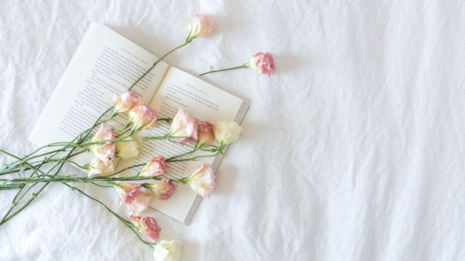 Libro abierto y flores sobre una cama de sábanas blancas