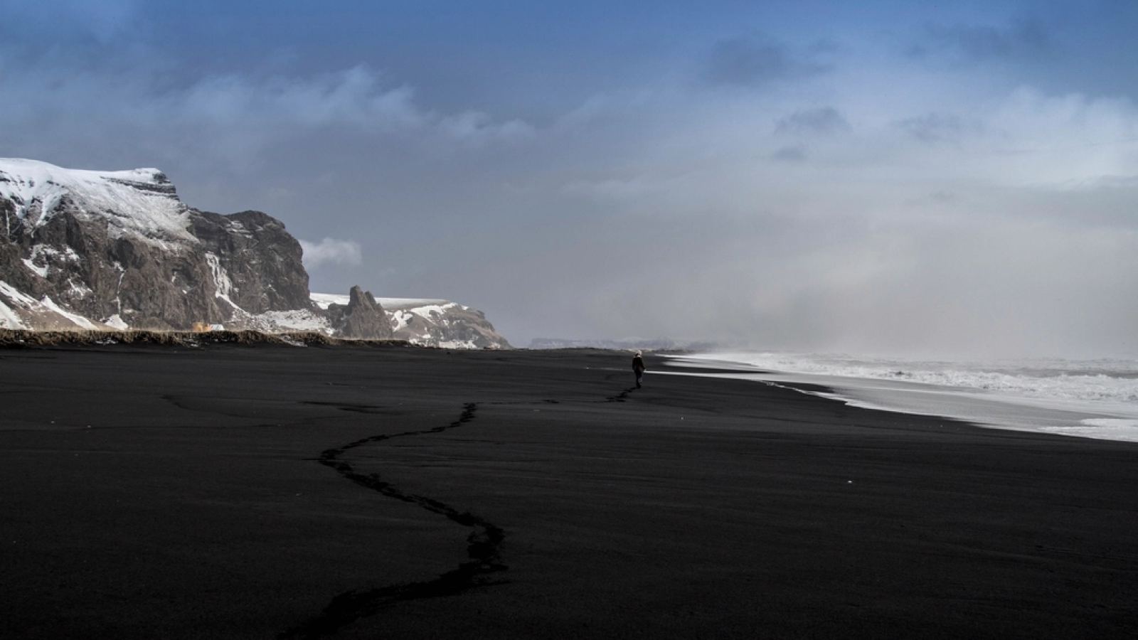 Playa de arena negra con una persona caminando a lo lejos